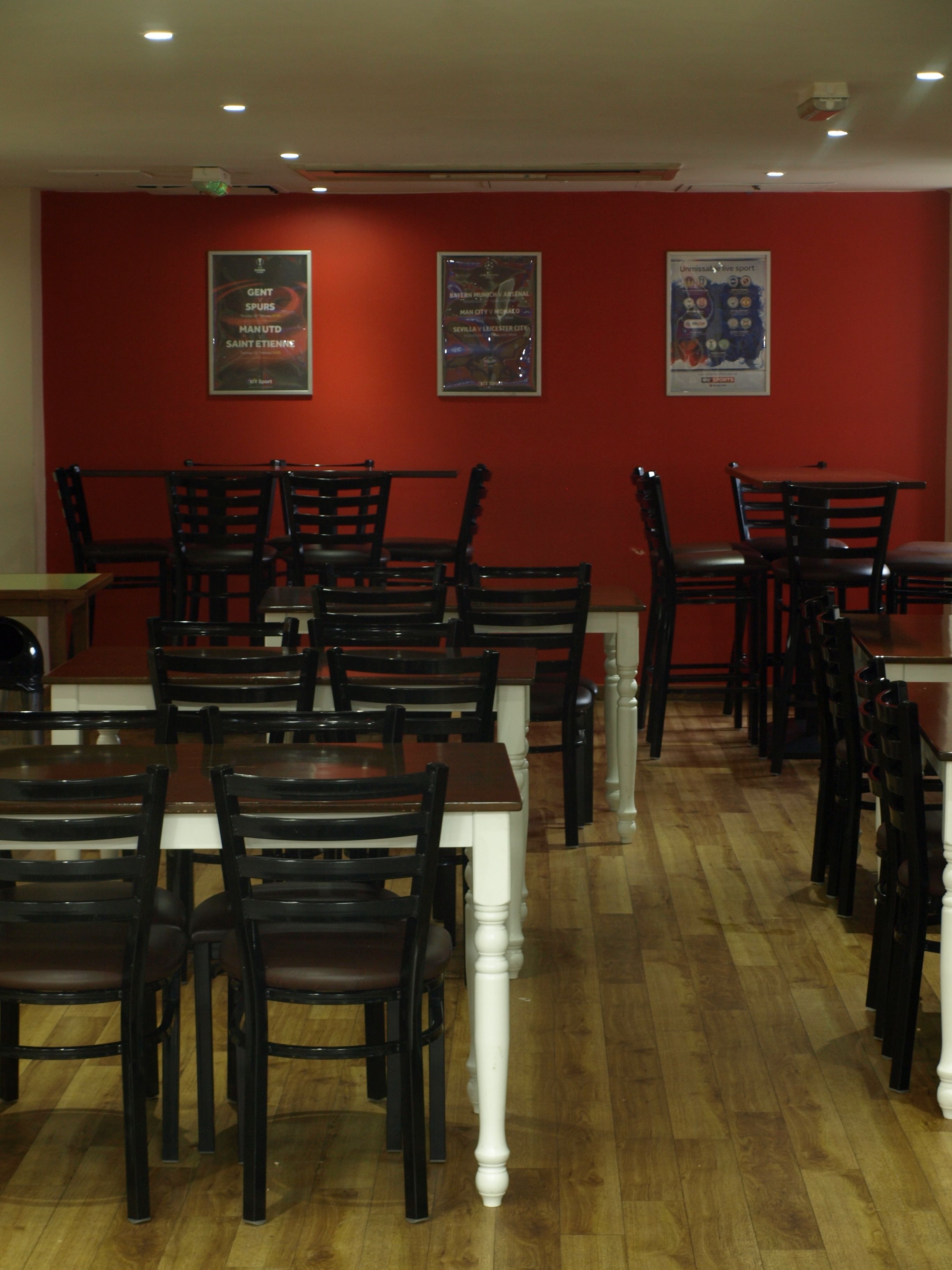L’intérieur d’un restaurant avec des murs rouges, des tables et des chaises en bois, et des affiches accrochées au mur.