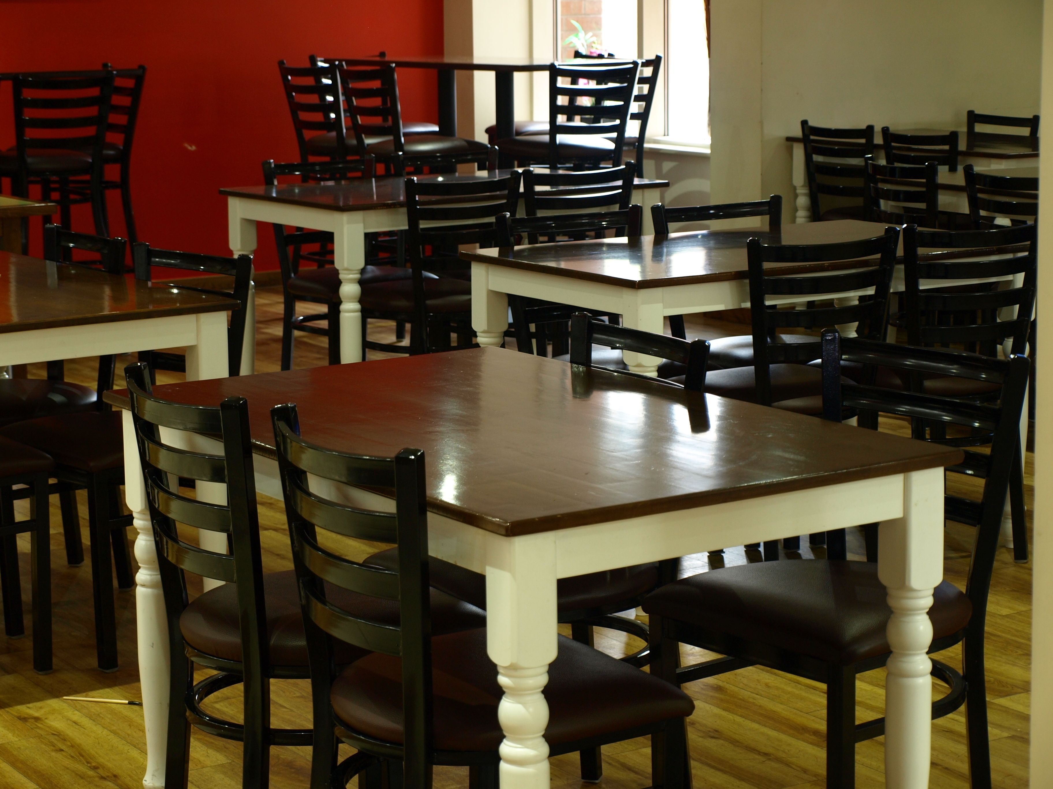A dining area with multiple tables and chairs, arranged in a spacious room with wooden flooring and a red accent wall.