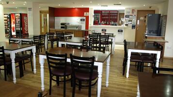 A restaurant with multiple dining tables and chairs, a counter with a beverage dispenser, and a television.
