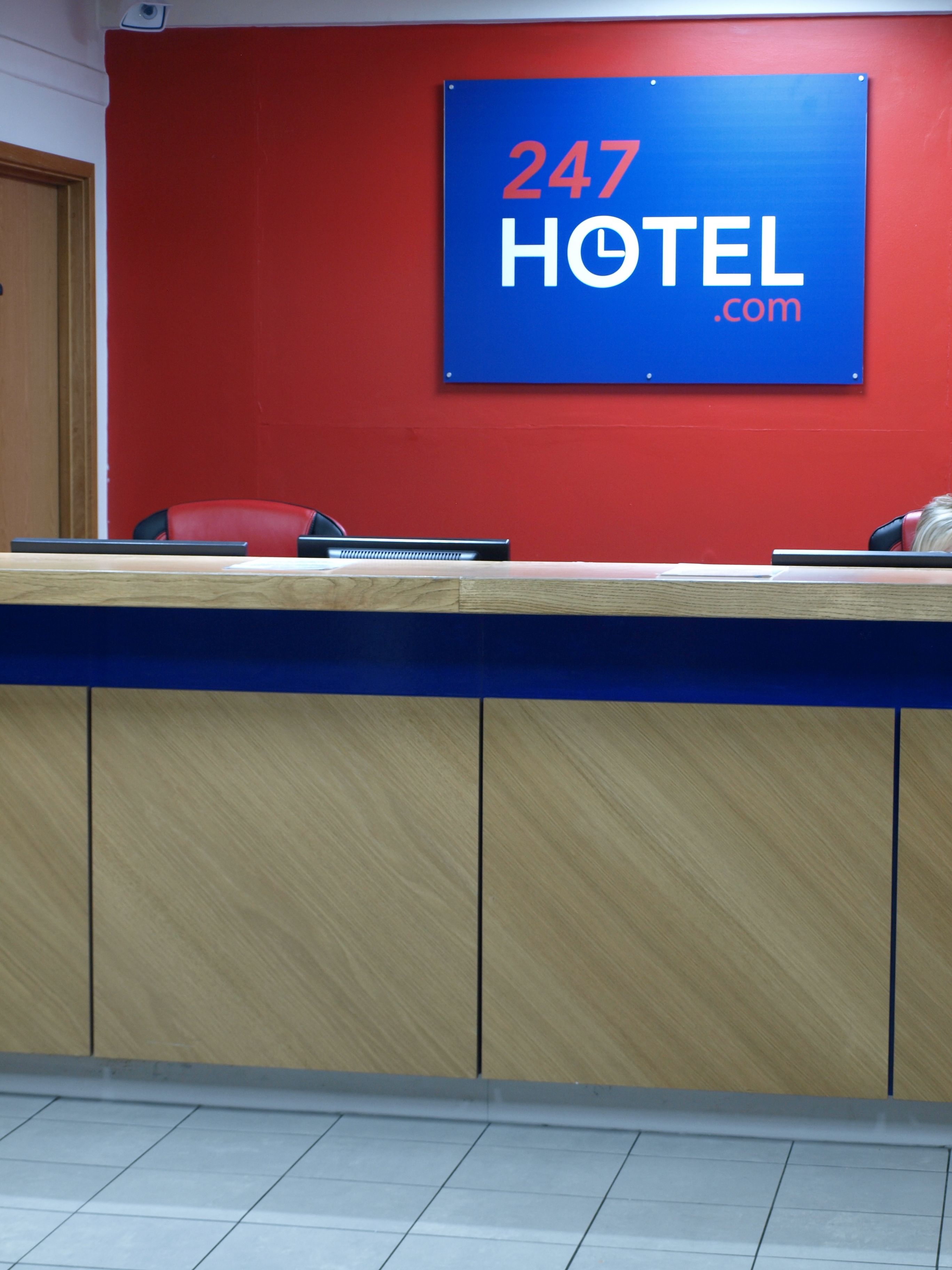 A reception desk with a sign reading "247 HOTEL.com" against a red wall.