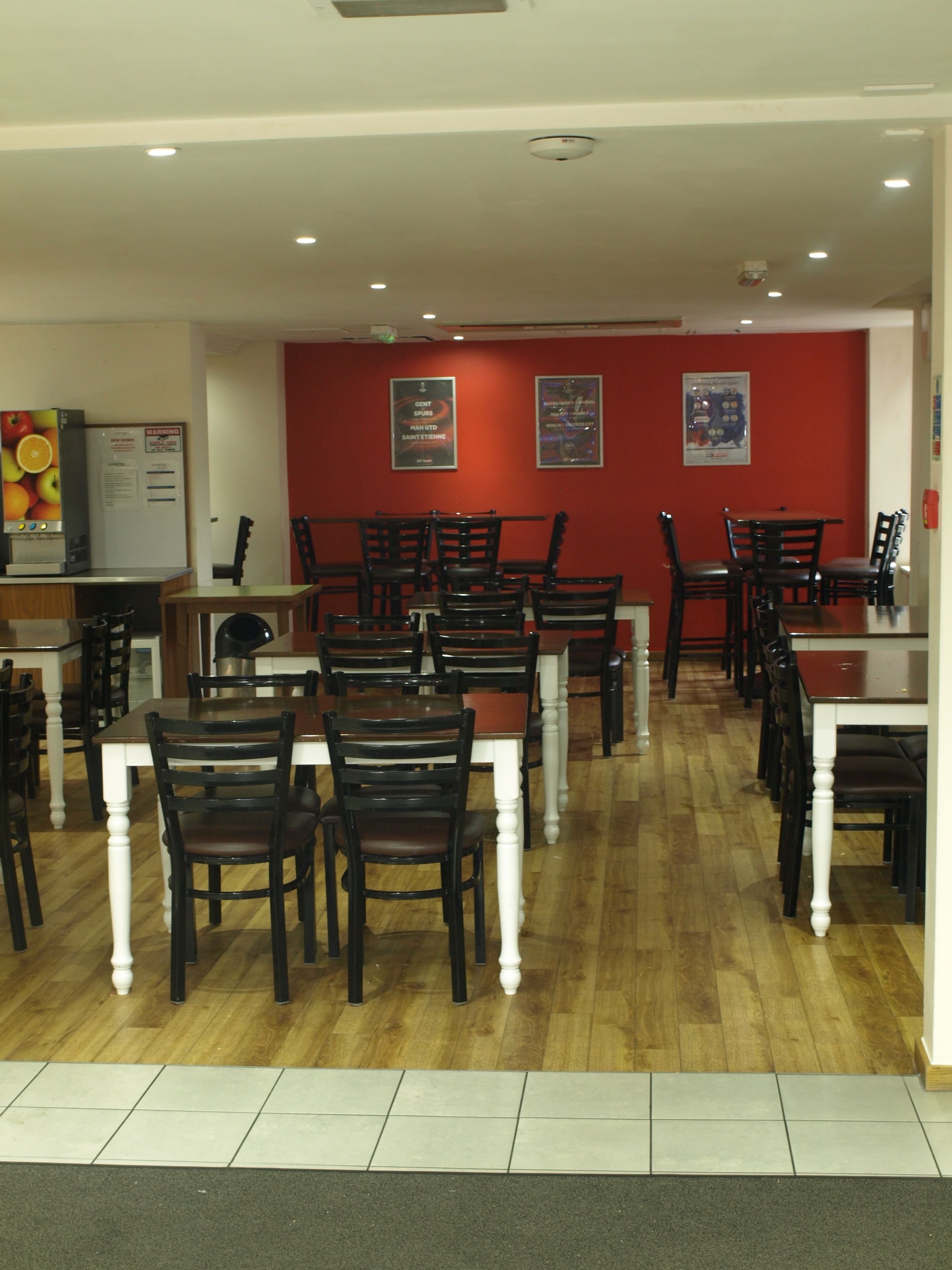 L’intérieur d’un restaurant présente de nombreuses tables et chaises, un mur d’accent rouge et un plafond doté d’un éclairage encastré.
