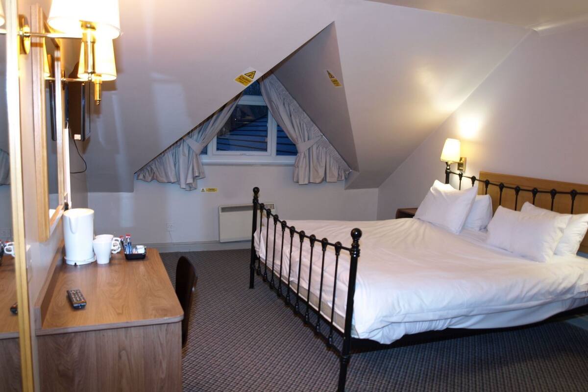 A hotel room with a bed, bedside table, lamp, and a window with curtains.