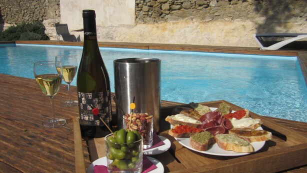A poolside table with a bottle of wine, glasses, a martini glass, a plate of bruschetta, and a glass of olives. - Hotel Château de Palaja (Palaja)