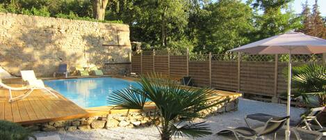 Ein Garten mit Pool, einer Holzterrasse, Liegestühlen und einer Palme.