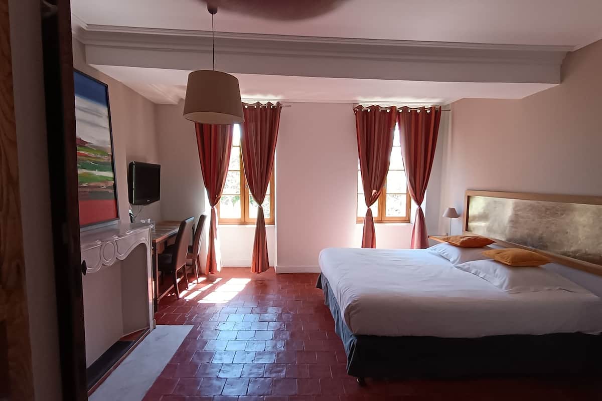 A bedroom with a bed, a desk, a television, and a window with curtains.