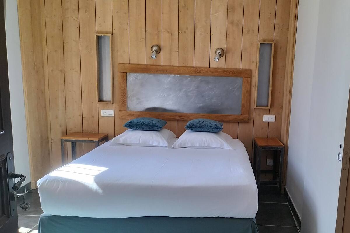 A bedroom with a wooden headboard, two bedside tables, a large mirror, and a bed with white bedding and blue pillows.