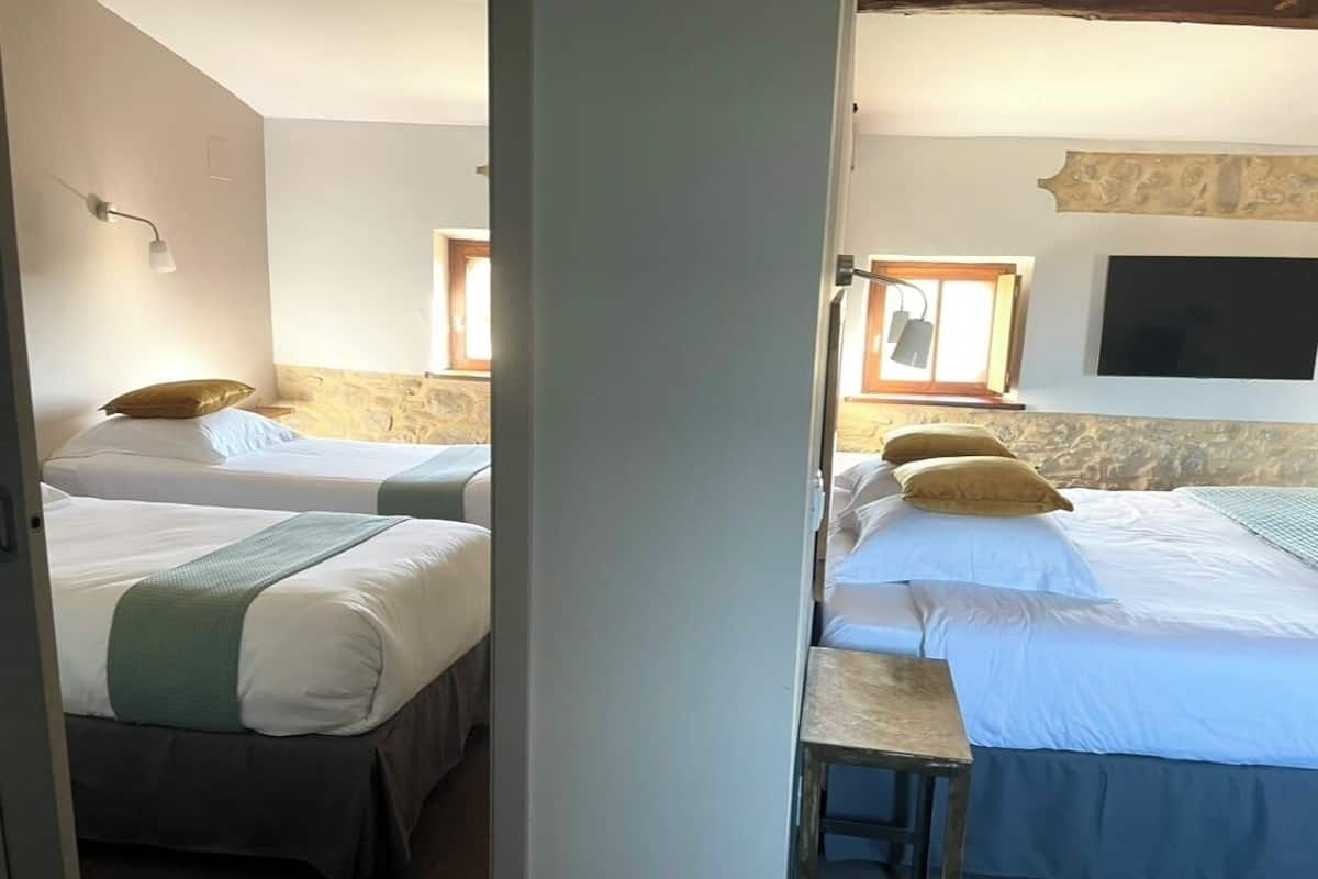 A room with two beds, a small table, and a TV mounted on the wall.