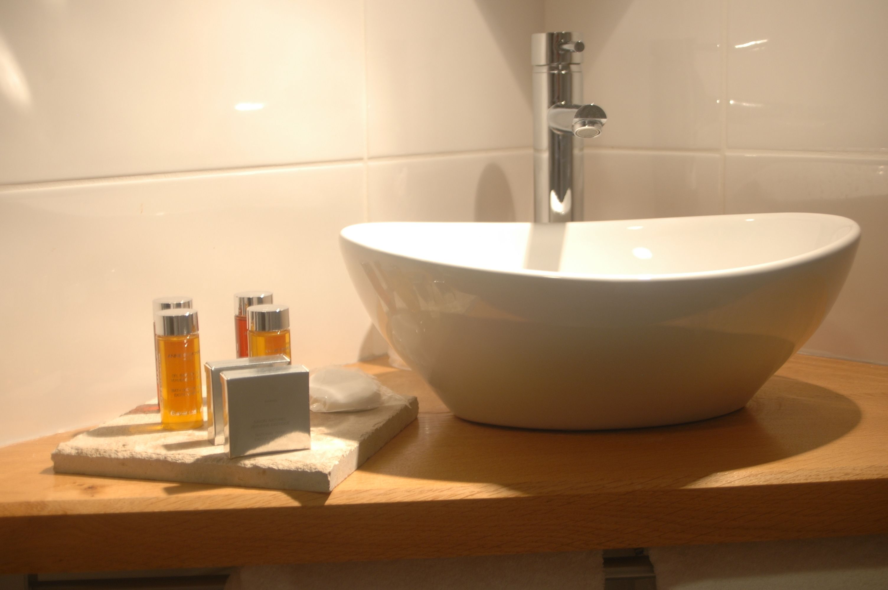 Un baño con un lavamanos blanco grande, un espejo y dos botellas de jabón líquido sobre una encimera de madera.