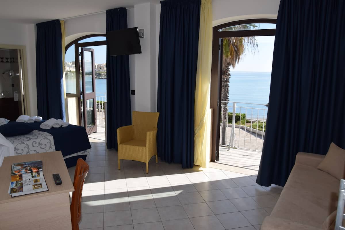 A hotel room with a balcony, a bed, a chair, and a TV.