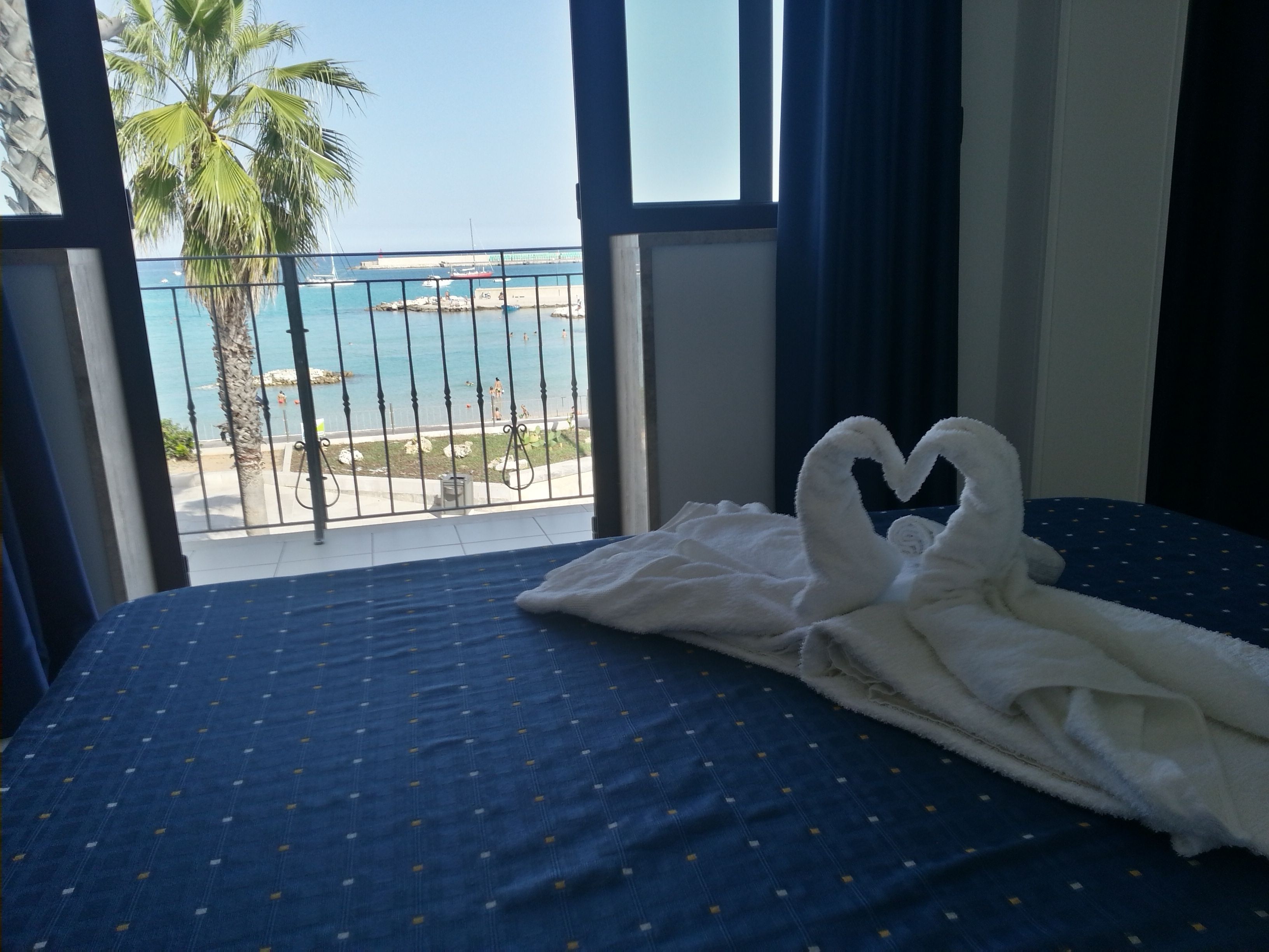A bed with a blue bedspread and a white towel shaped like swans on it.