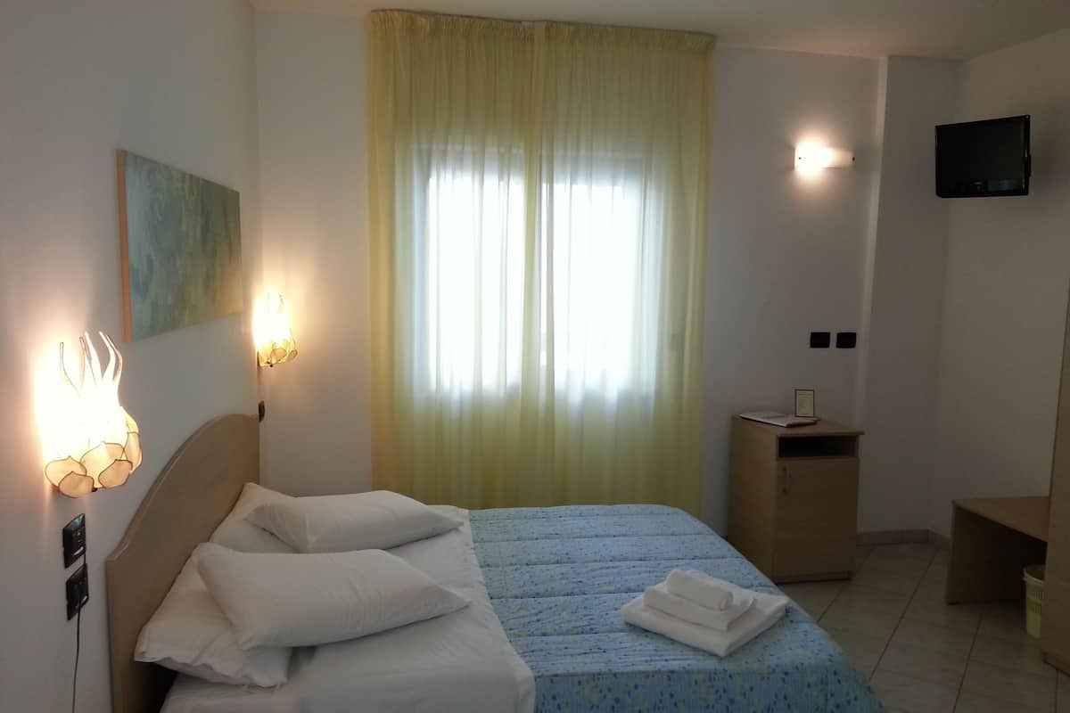 A neatly made bed with white linens, a bedside table with a lamp, and a window with curtains.
