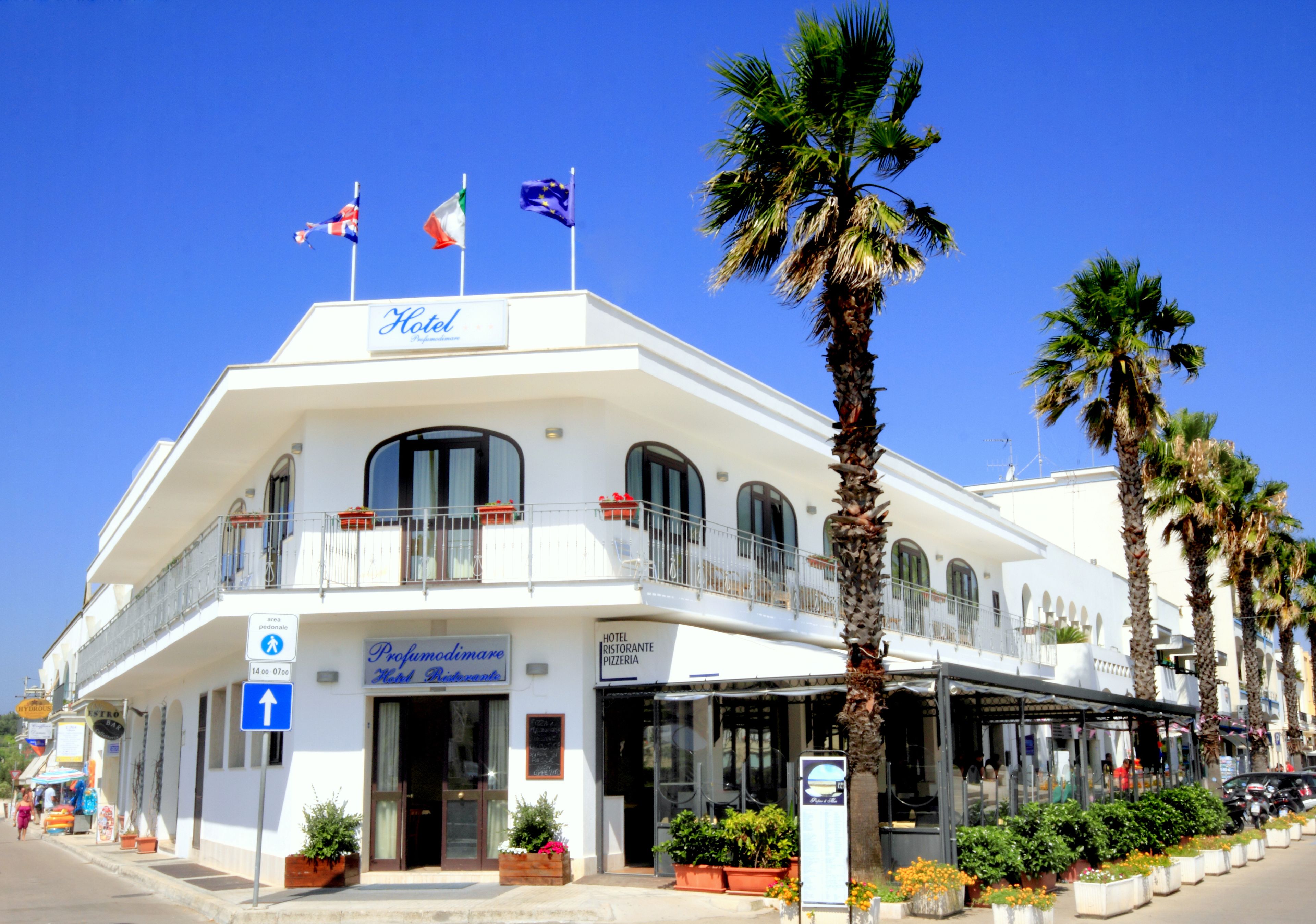 A white hotel with a balcony, a restaurant, and a pizzeria on the ground floor.