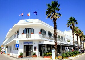 A white hotel with a balcony, a restaurant, and a pizzeria on the ground floor.
