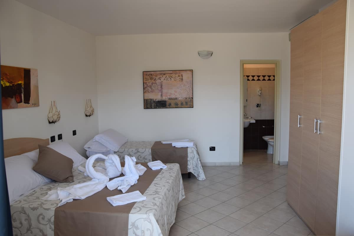 A hotel room with two beds, a bathroom, and a hallway.