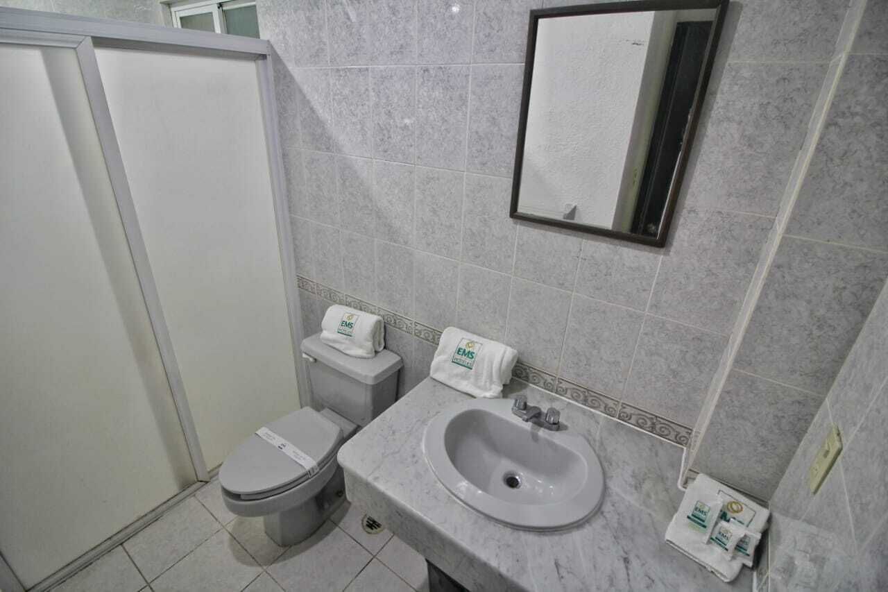 Un baño con inodoro, lavabo y espejo. Hay toallas sobre el lavabo y el inodoro.