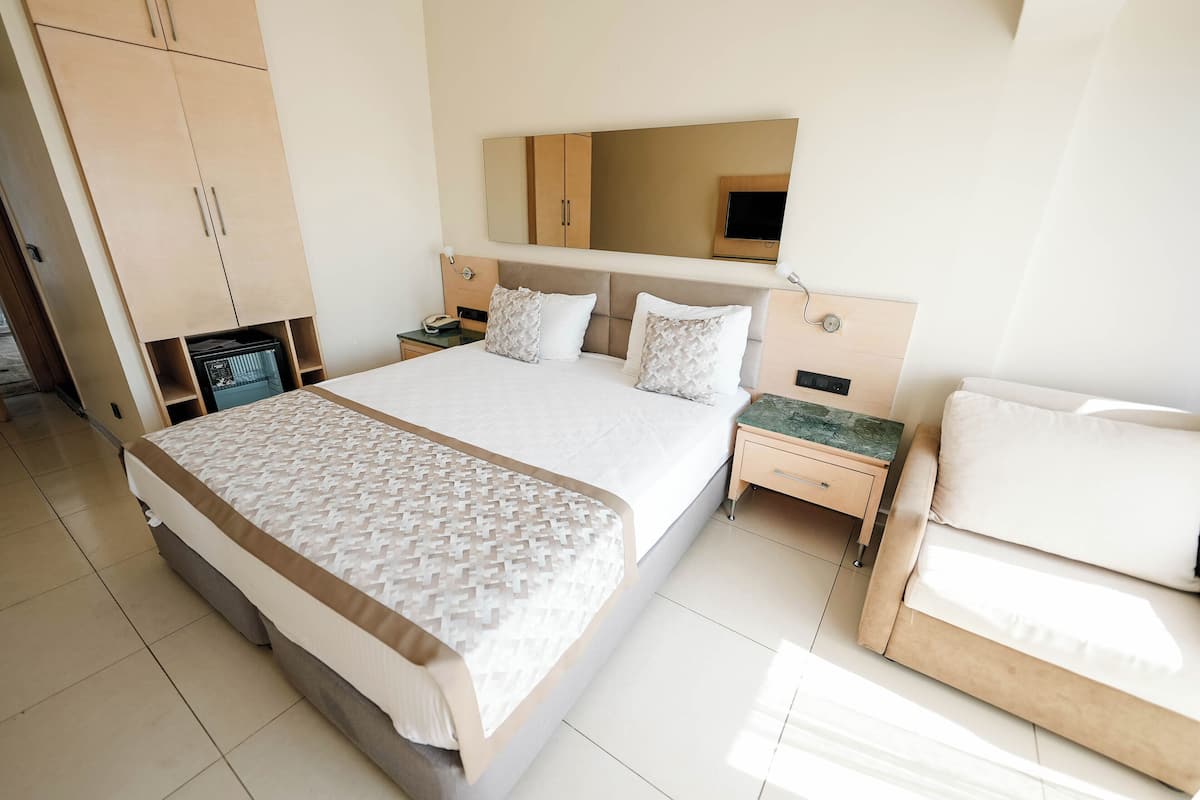 A hotel room with a large bed, a bedside table, a nightstand, a wardrobe, and a mirror.