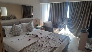 A hotel room with a bed, a nightstand, a chair, a desk, and a large window with curtains. - Marin-A Hotel (Bodrum)