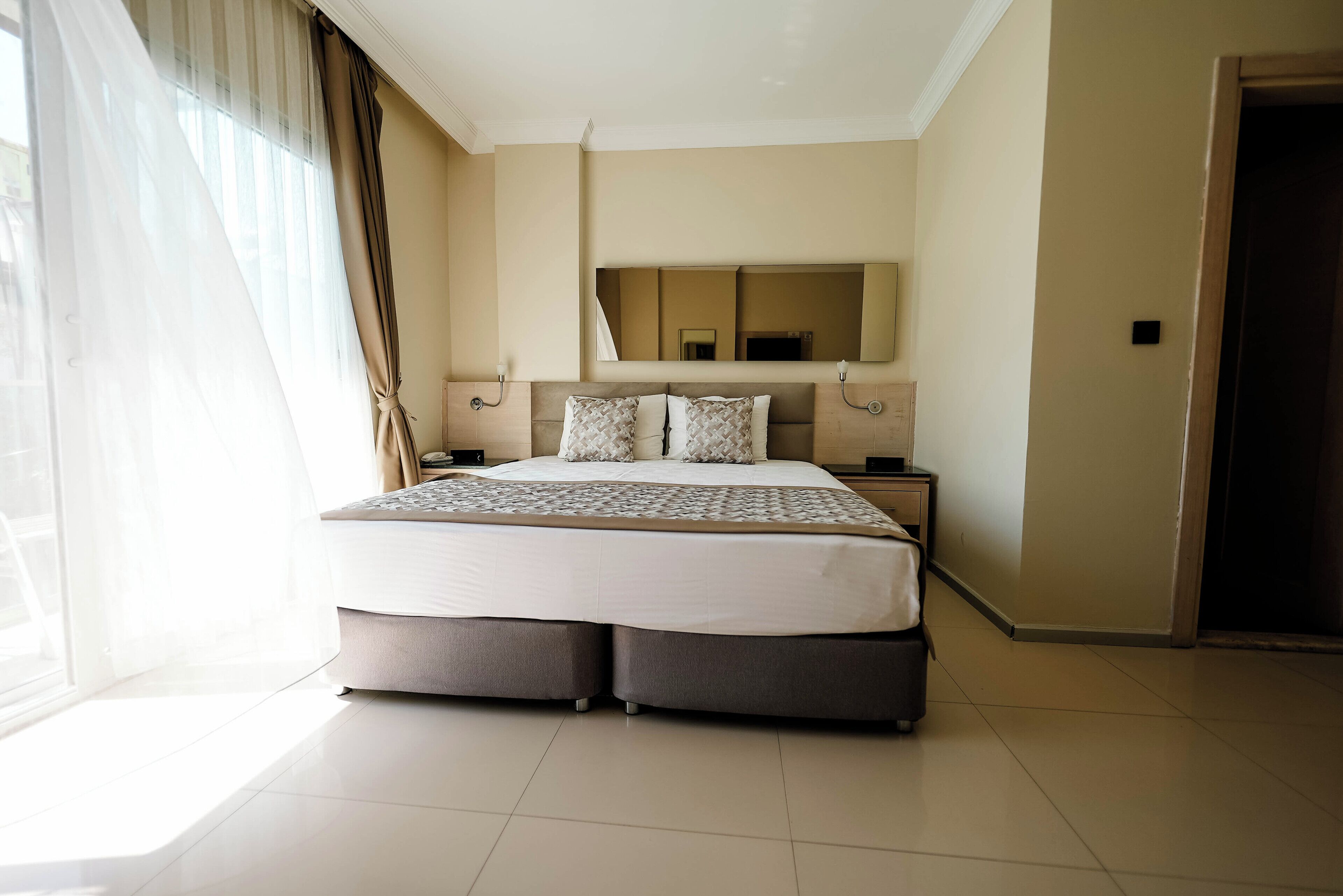 Una habitación de hotel moderna con una cama grande, una mesita de noche, un espejo y una puerta corredera de vidrio.