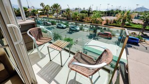 A balcony with wicker chairs, a glass table, and a view of a parking area with cars and palm trees. - Marin-A Hotel (Bodrum)