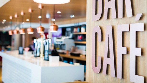 A modern cafe interior with a wooden counter and hanging pendant lights. - Travelodge London Vauxhall (London)