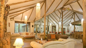 A spacious living area with a high ceiling, wooden beams, and a large window providing natural light. Furnishings include sofas and a coffee table. - Gorilla Safari Lodge (Bwindi)