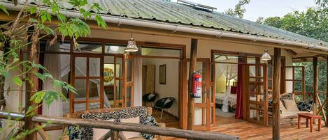 A wooden deck with a sofa and chairs, a fire extinguisher, and a view of the surrounding trees.