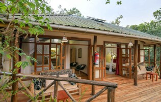Une terrasse en bois avec un canapé et des fauteuils, un extincteur et une vue sur les arbres environnants.