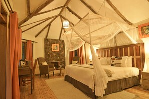 A bedroom with a four-poster bed, a stone wall, a wooden ceiling, and a small table with a lamp. - Gorilla Safari Lodge (Bwindi)