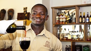 A person pouring red wine into a glass at a bar with shelves of various bottles in the background. - Gorilla Safari Lodge (Bwindi)