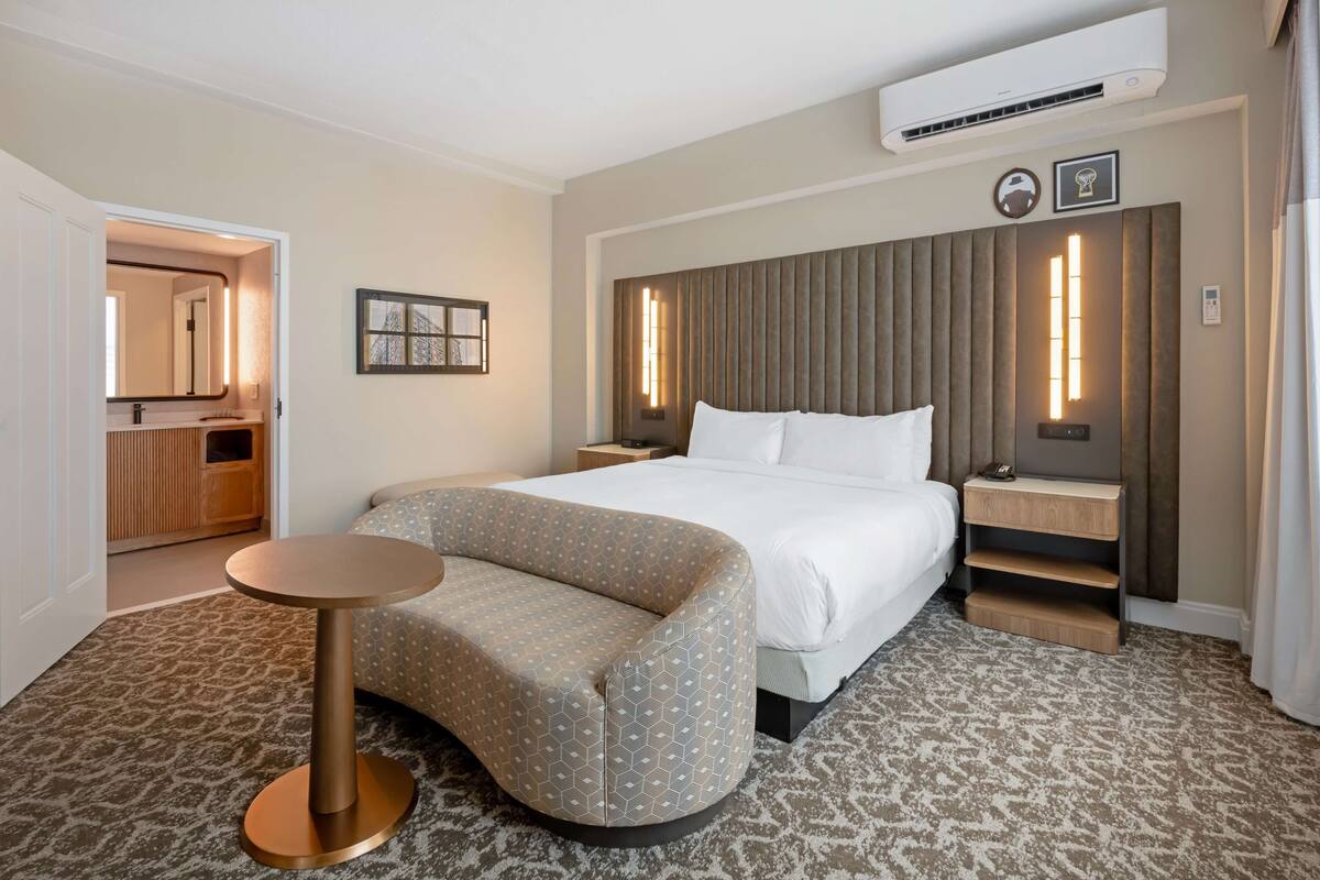 Een hotelkamer met een bed, een ronde tafel, een bank, een nachtkastje en een spiegel.