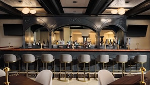 Een bar met een spiegelwand, meerdere barkrukken en een divers assortiment aan flessen en glazen.
