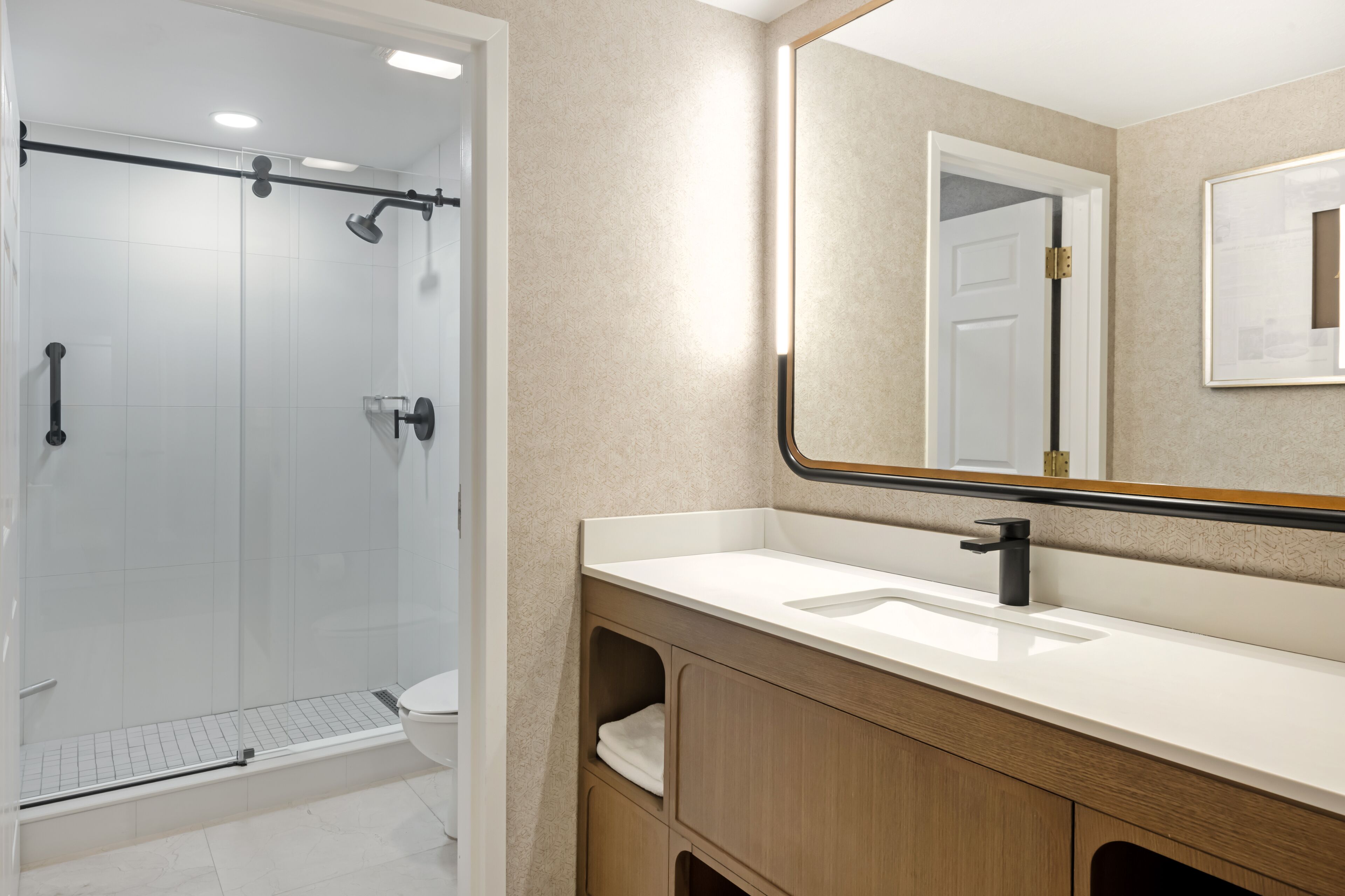 A modern bathroom with a glass-enclosed shower, a white sink, and a wooden vanity.