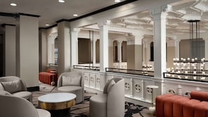 Een moderne hotel lobby met een ronde salontafel, een zithoek en een grote spiegel die de ruimte weerspiegelt.