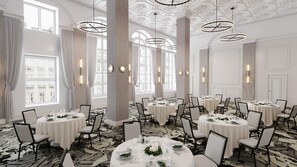 Un comedor de hotel con varias mesas redondas dispuestas para comer, ventanas amplias e iluminación decorativa.