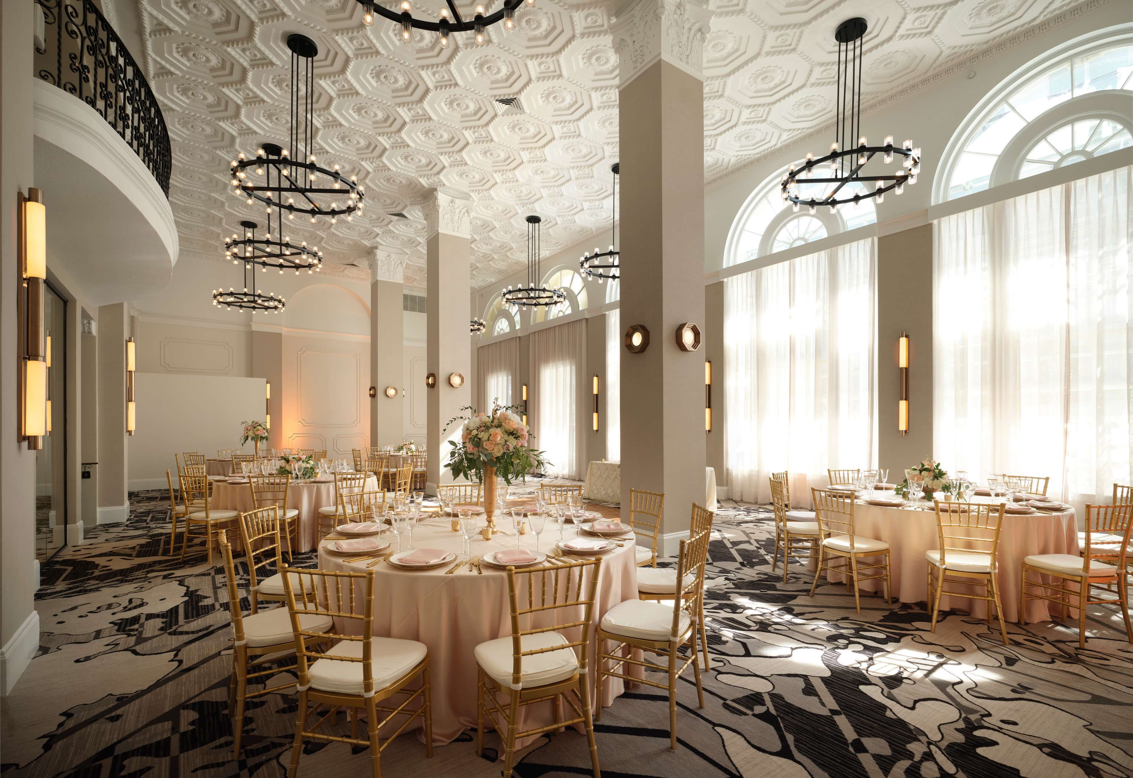 Une salle de banquet avec des tables rondes, des chaises dorées et des lustres.