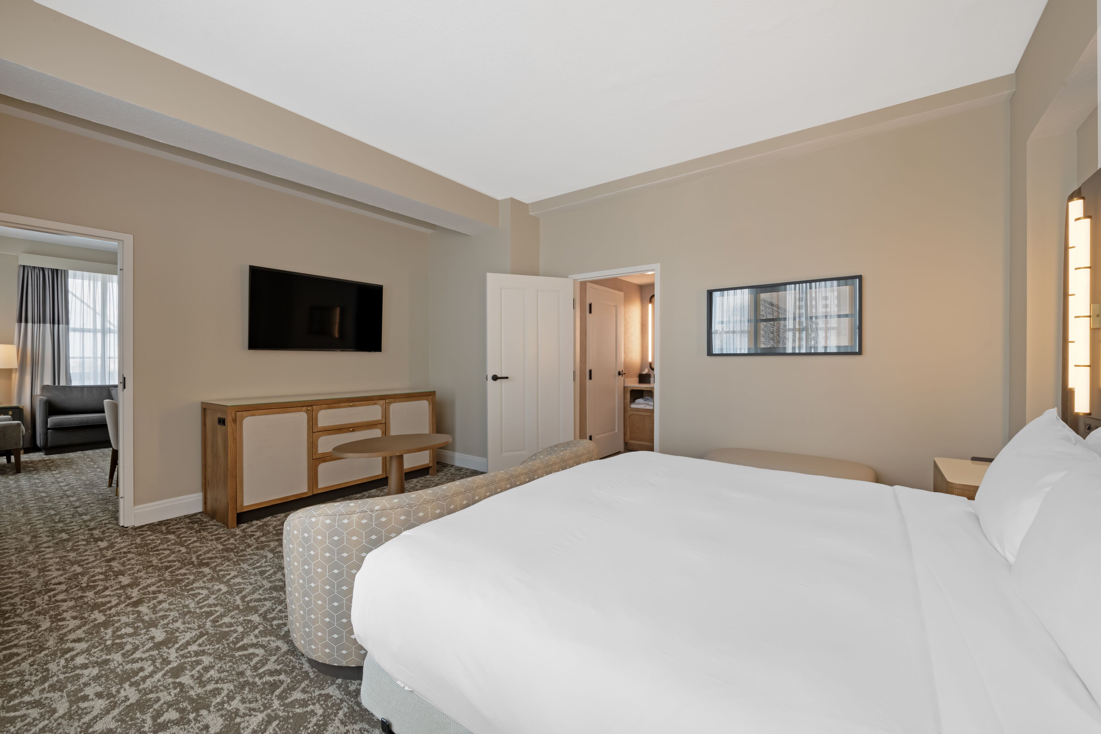 A hotel room with a large bed, a desk, a TV, and a door leading to another room.