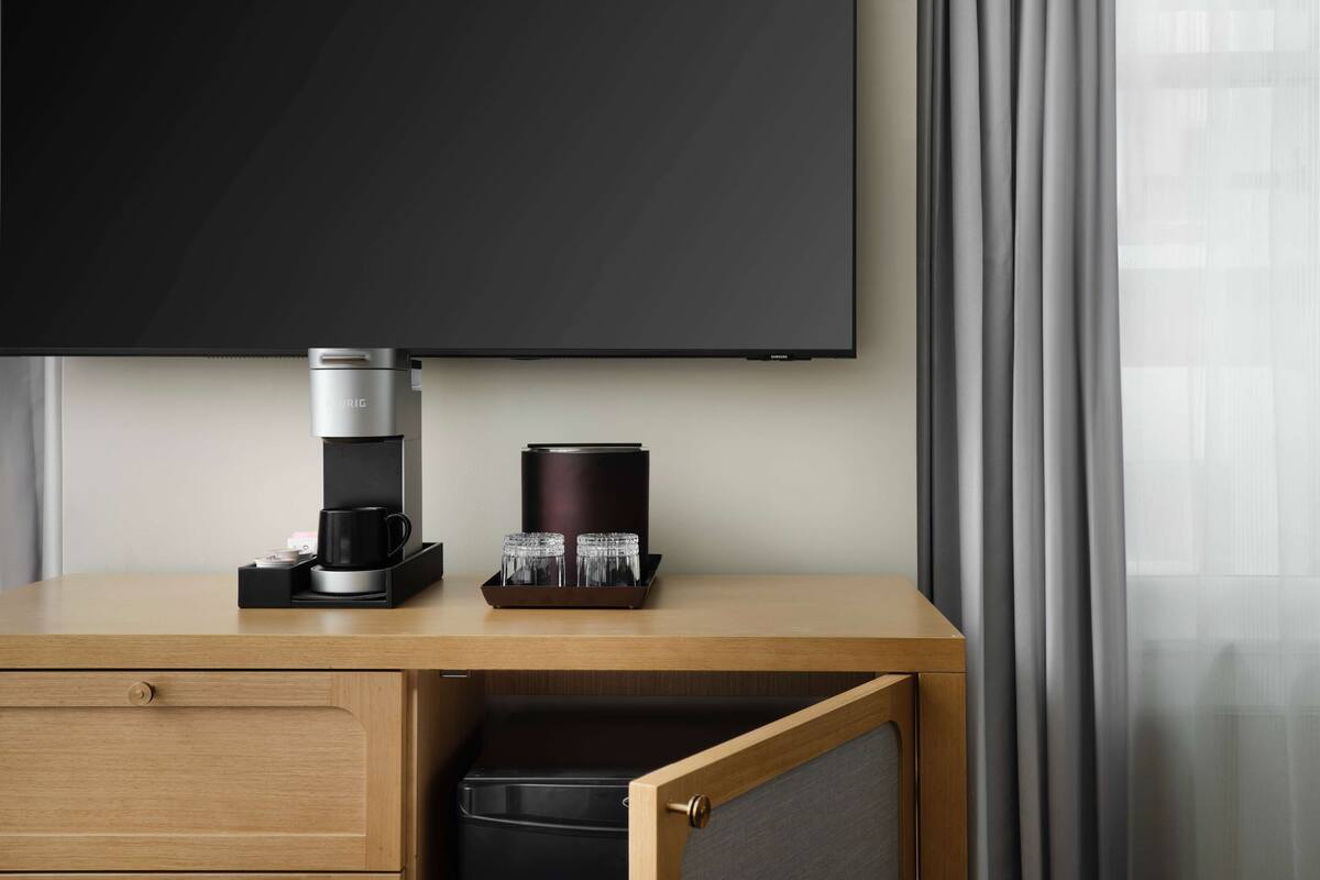 Een hotelkamer met een flatscreen-tv aan de muur, een koffiezetapparaat en een dienblad met glazen op een houten bureau.
