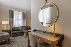 A hotel room with a sofa, a desk with a mirror, a lamp, and a view of the outdoors. - Hotel Flor Tampa Downtown, Tapestry Collection by Hilton (Tampa)