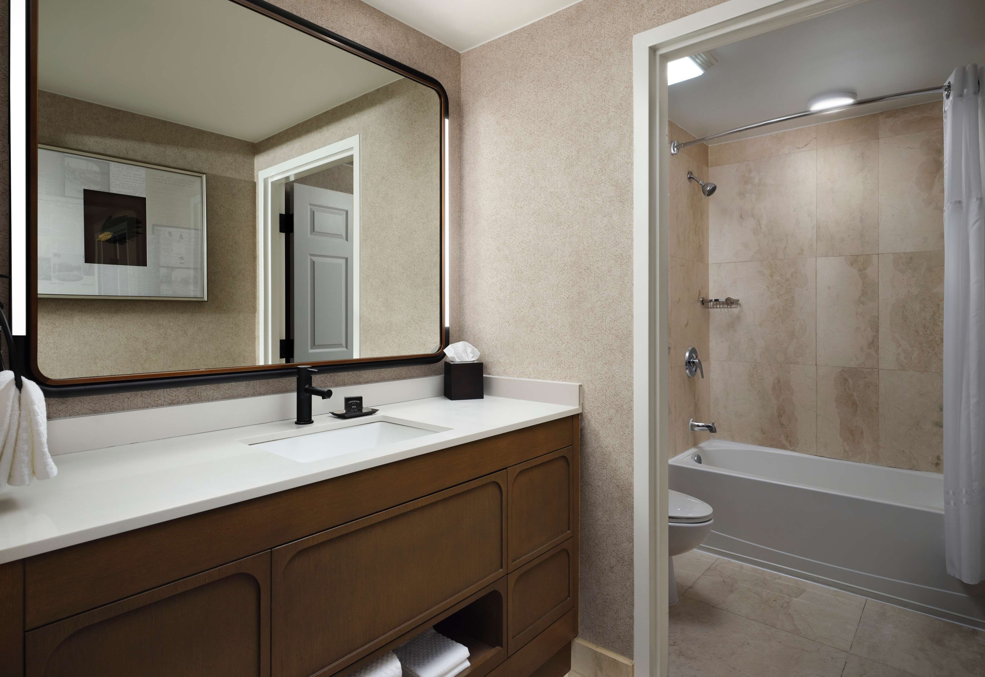 A bathroom with a double sink vanity, a large mirror, a shower, and a toilet.