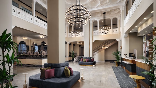 Een ruime lobby met een weelderige kroonluchter, een receptiebalie en een zithoek met een bank en fauteuils.