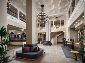 Een ruime lobby met een weelderige kroonluchter, een receptiebalie en een zithoek met een bank en fauteuils.