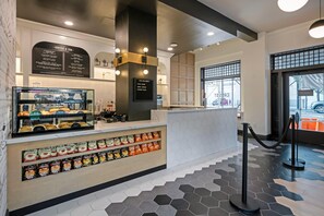 Interior de una cafetería con un menú, una variedad de pasteles y una barra con aperitivos.