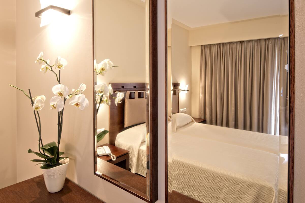 Habitación de hotel con un espejo grande, una orquídea en maceta, una mesita de noche con teléfono y una cama bien hecha.