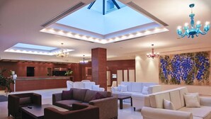 A spacious lobby with a high ceiling, skylights, and modern chandeliers. - Kymi Palace Hotel (Kymi-Aliveri)