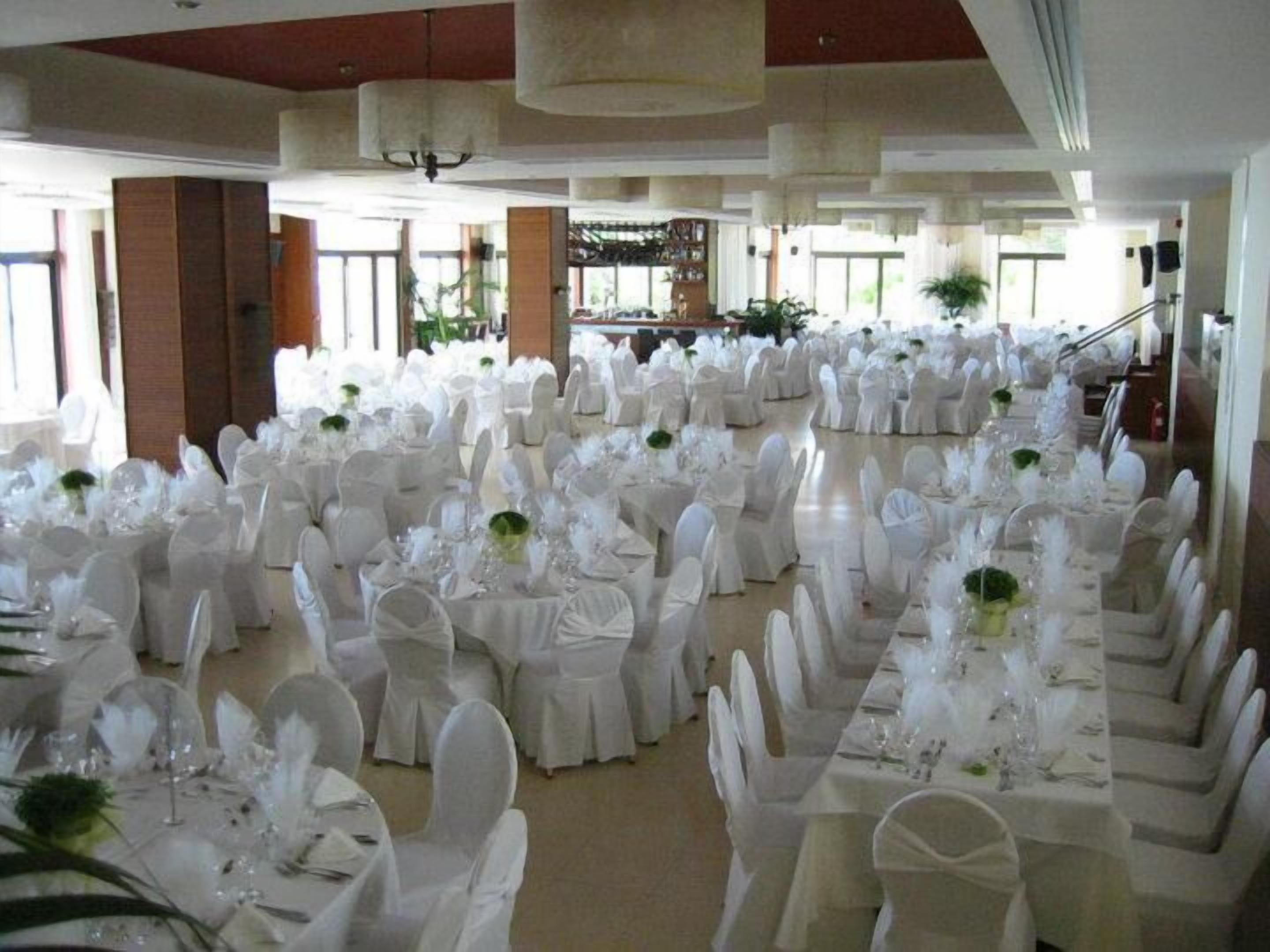 Un salón de banquetes con filas de mesas redondas, cada una cubierta con mantel blanco, sillas blancas y centros de mesa.