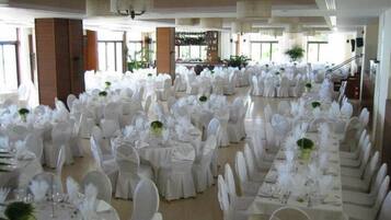 Un salón de banquetes con filas de mesas redondas, cada una cubierta con mantel blanco, sillas blancas y centros de mesa.