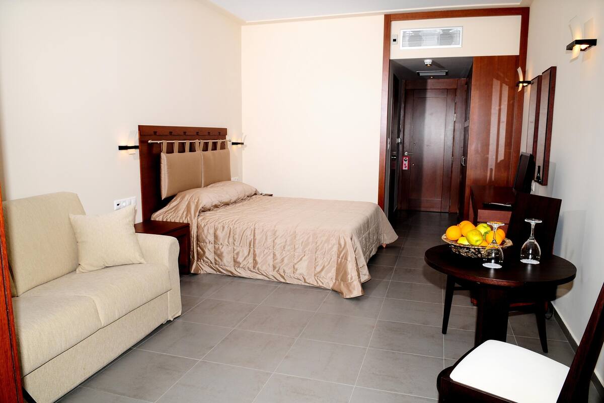 Una habitación de hotel con cama, sofá, una mesa de comedor con fruta y una silla.