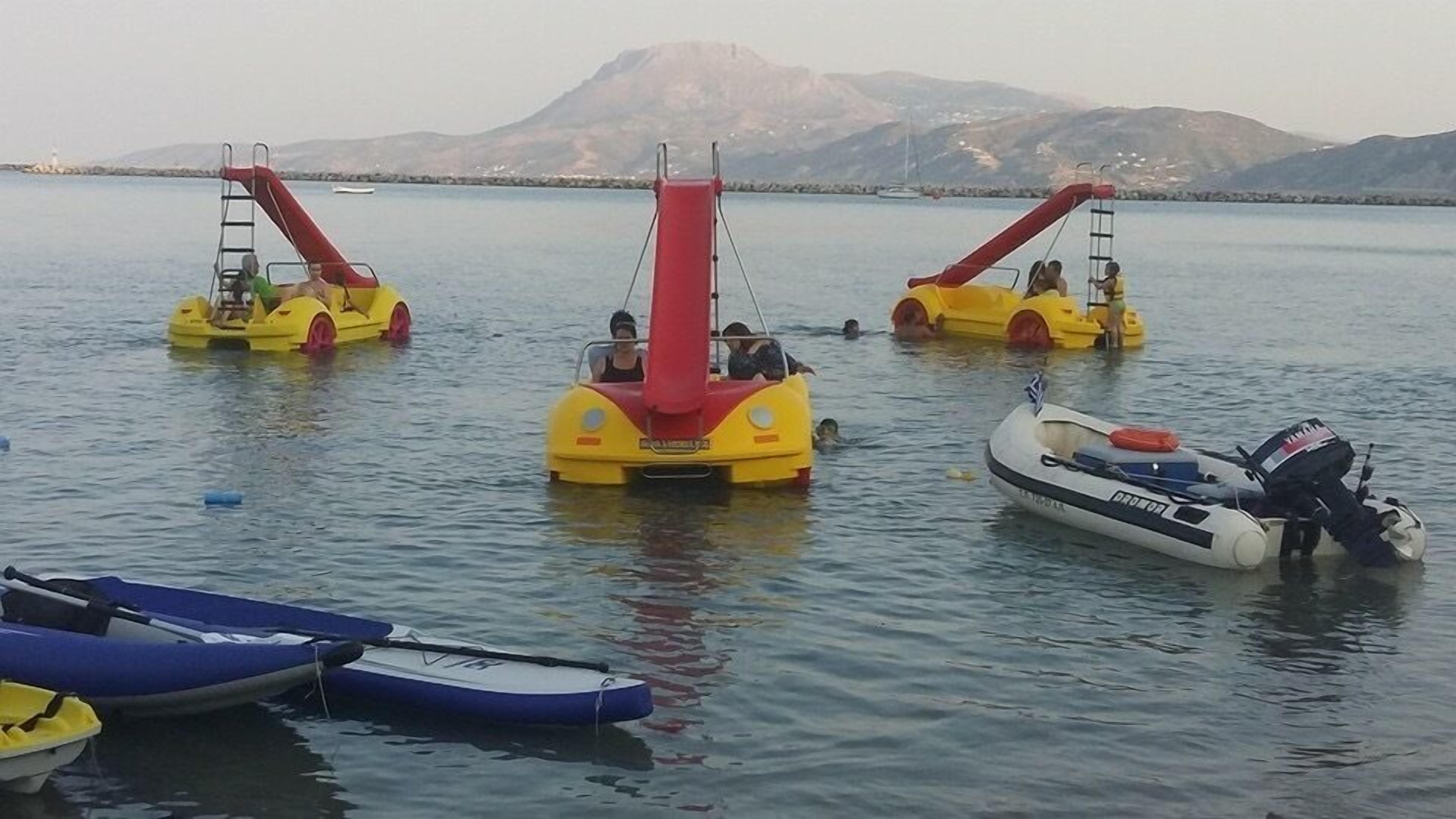 Un cuerpo de agua con varias embarcaciones, incluyendo un bote inflable amarillo y rojo, un motorboat blanco y un kayak azul.