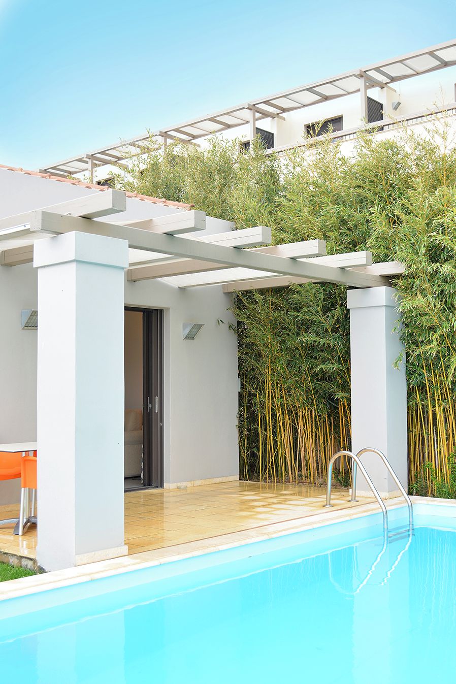 Un área de piscina moderna al aire libre con un pérgola, una terraza de madera y un fondo de bambú.