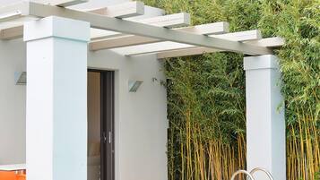 Un área de piscina moderna al aire libre con un pérgola, una terraza de madera y un fondo de bambú.
